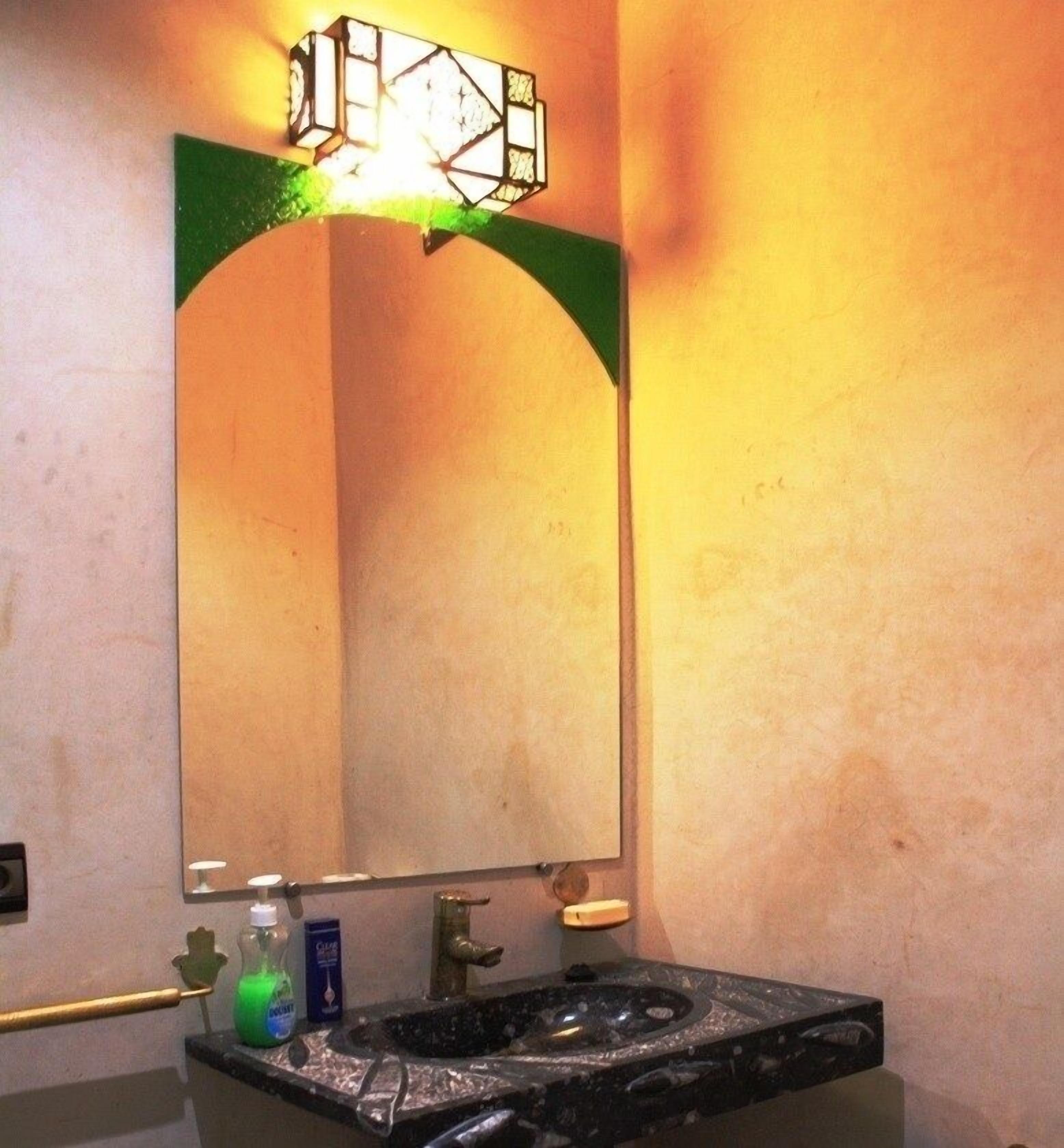 Une salle de bain avec un lavabo en marbre noir, un miroir encadré de vert et un luminaire fixé au mur.