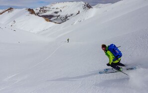 A person skiing down a snowy slope with a mountain in the background. - Riad Jnane Imlil (Asni)