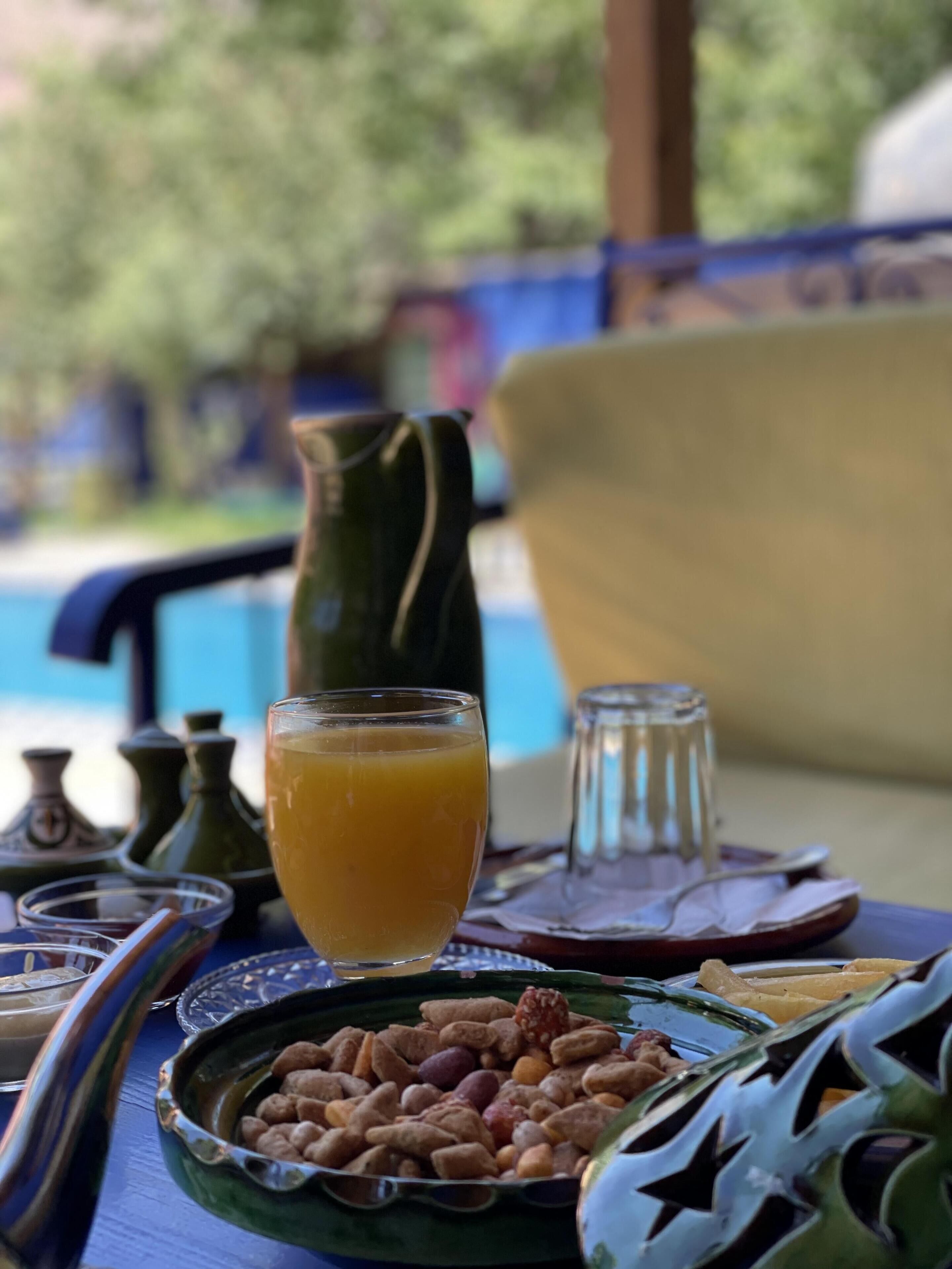 Una mesa de comedor con un vaso de jugo de naranja, un plato de nueces y una jarrón.