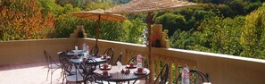 An outdoor dining area with a round table and chairs, an umbrella, and a view of the surrounding greenery. - Riad Jnane Imlil (Asni)