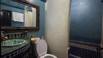Un baño con suelo de baldosas azules y blancas, un inodoro blanco, un lavabo con lavamanos verde y un espejo con marco de madera.