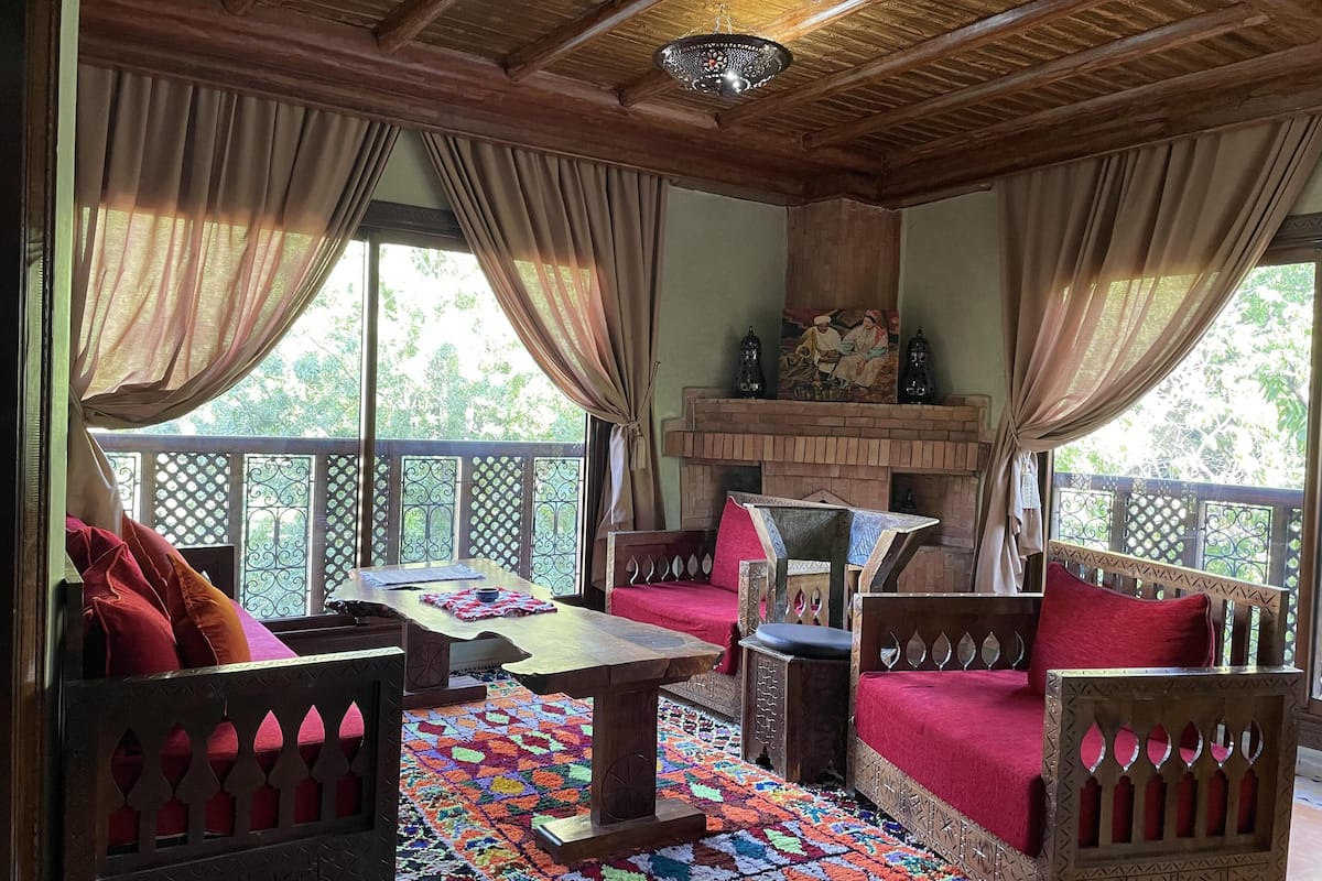 Quarto tradicional com teto de madeira, carpete estampado e lareira.