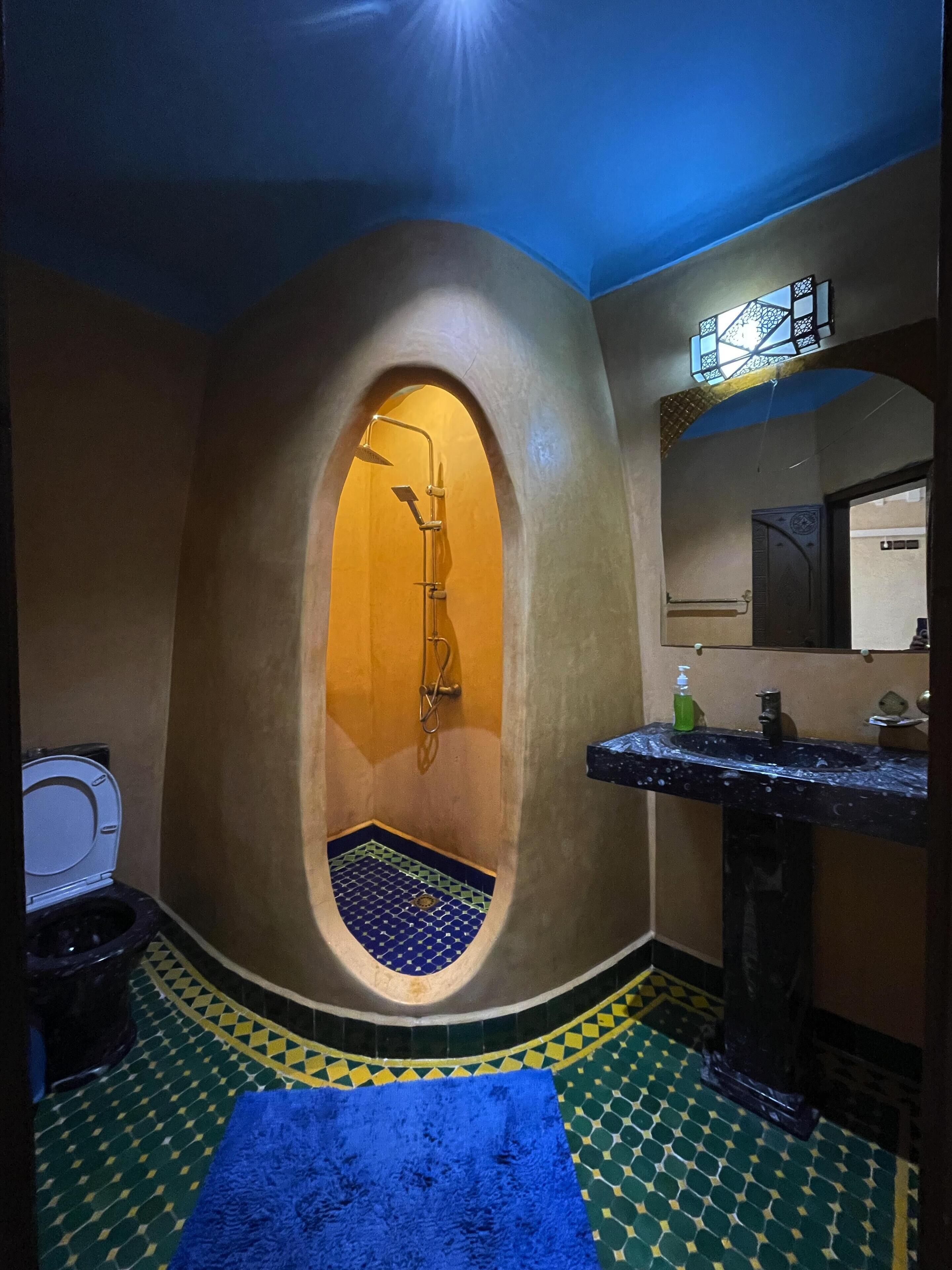 Un baño con un box de ducha de diseño curvo, un lavamanos con encimera de mármol y un suelo estampado.