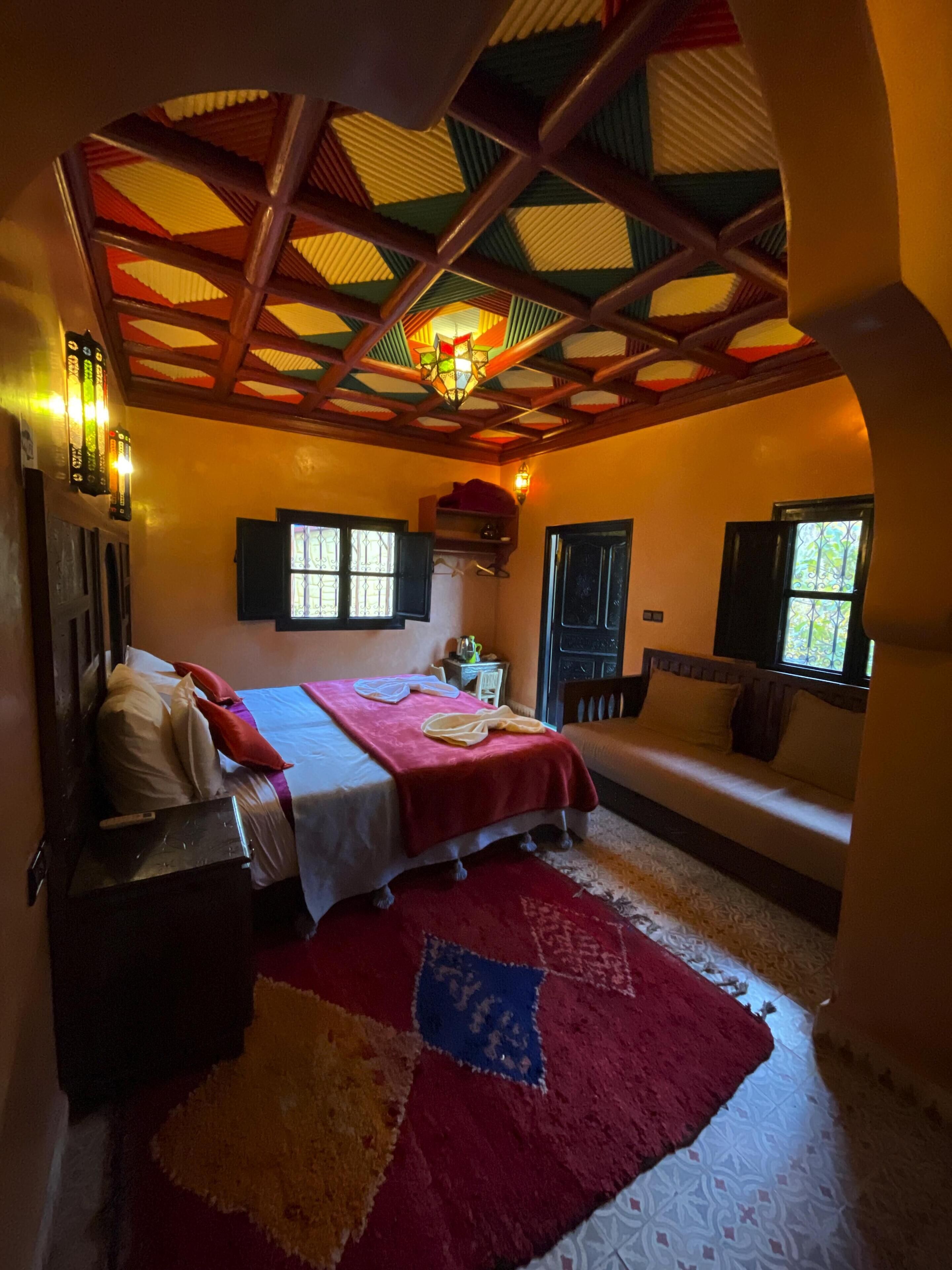A cozy bedroom with a bed, a sofa, a small table, and a decorative ceiling.