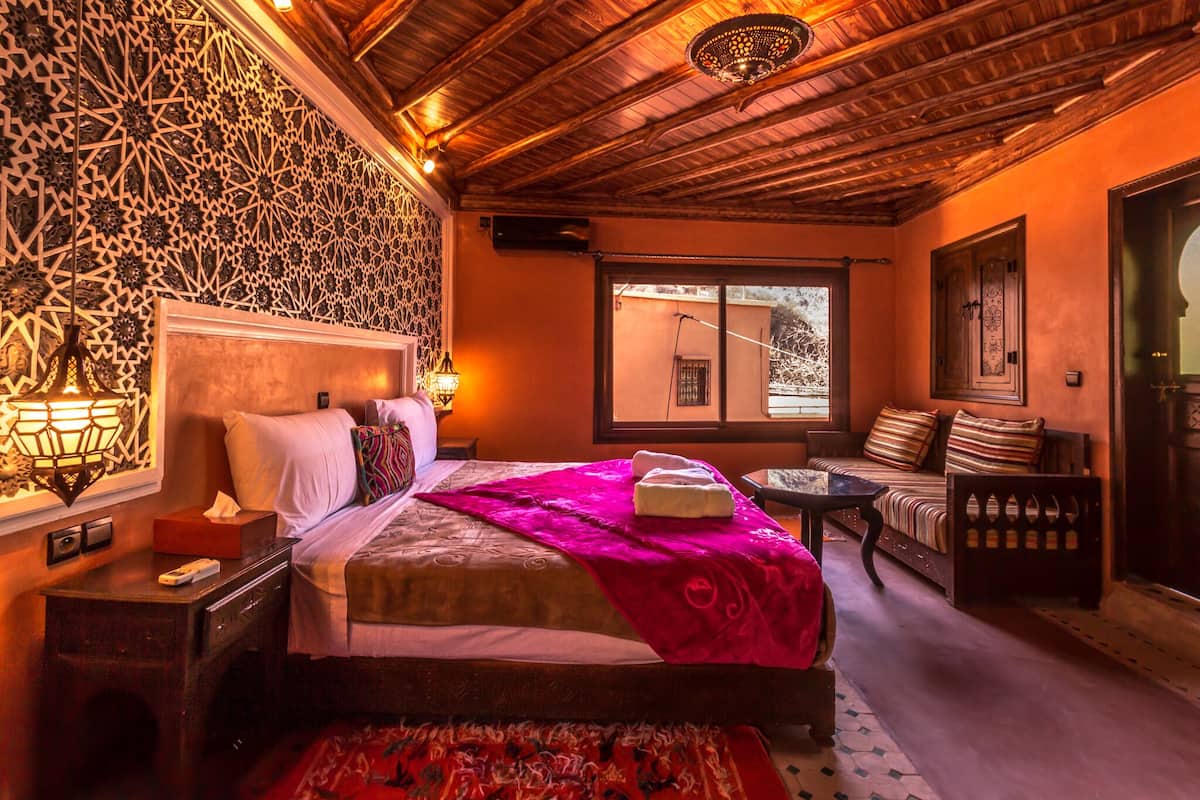 Quarto com cama, mesa de cabeceira, abajur e vista para o exterior.