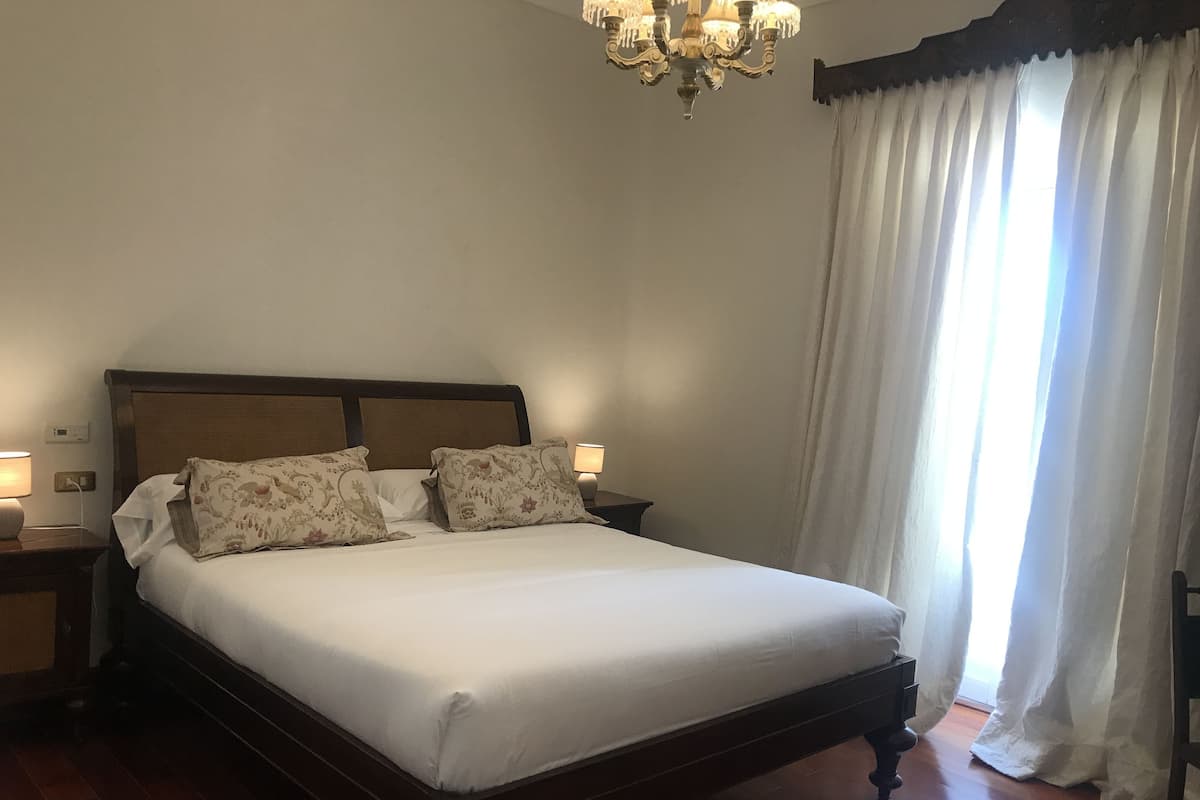Uma cama bem arrumada com almofadas florais, uma cabeceira de madeira e um candelabro acima.