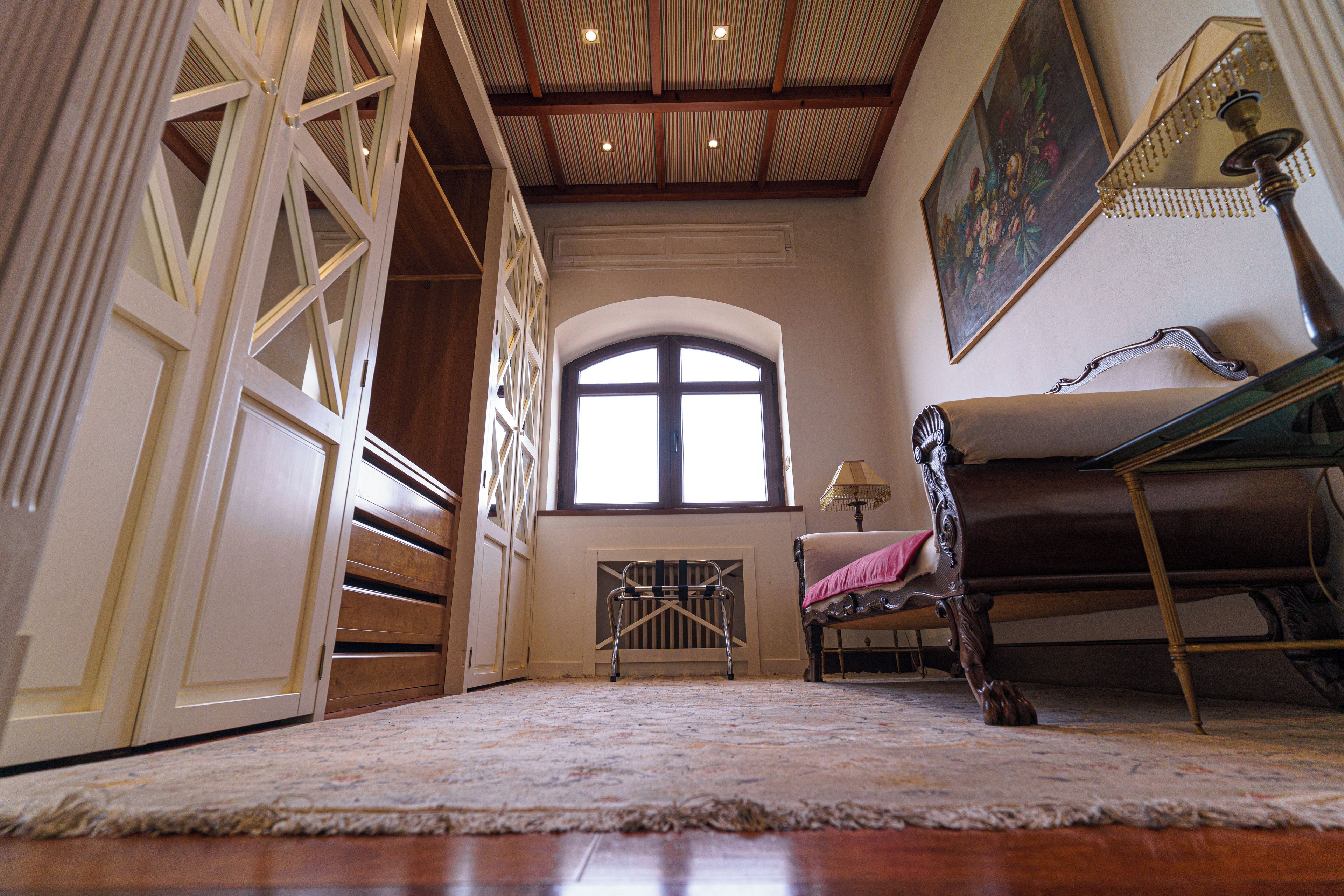 Una habitación con un gran ventanal arqueado, suelo de madera y una silla con cojín.