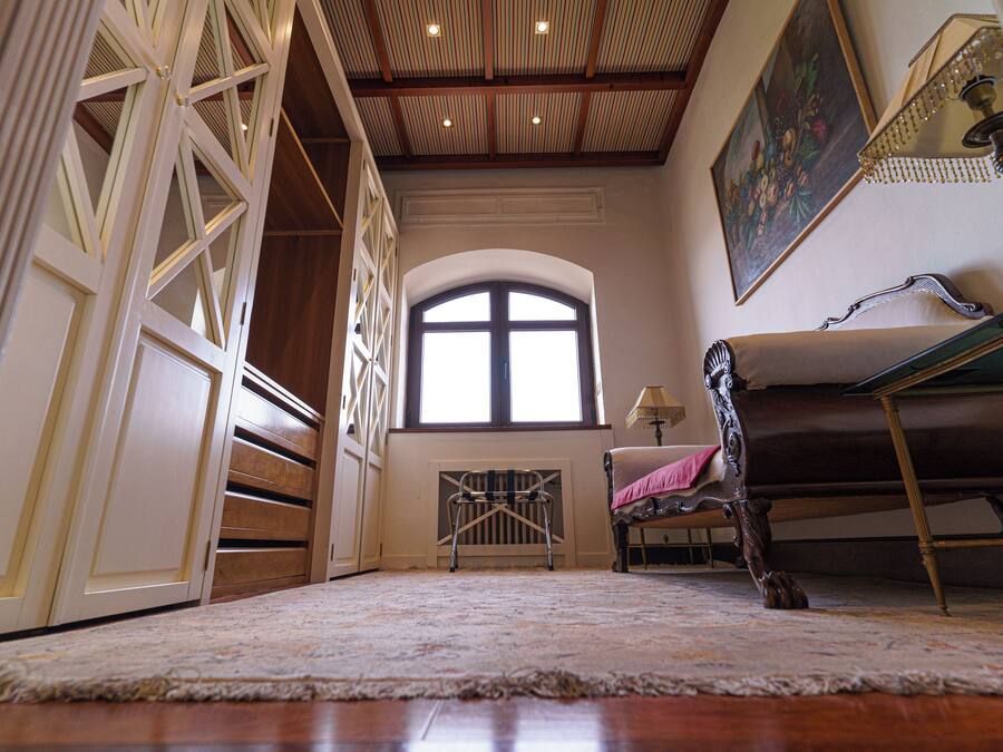 Una habitación con un gran ventanal arqueado, suelo de madera y una silla con cojín.