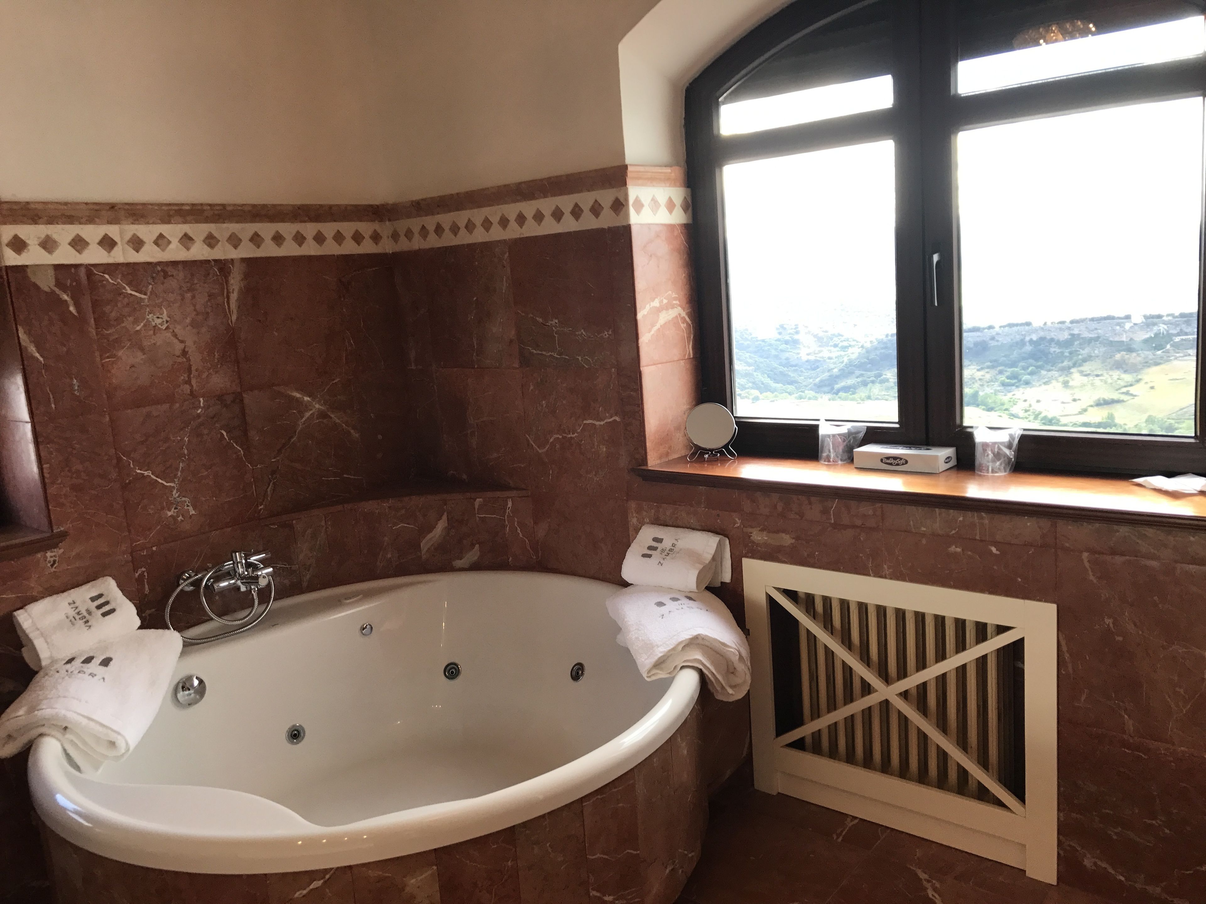 Un baño con una bañera grande, una ventana que ofrece vistas al campo y un perchero con toallas.