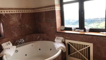 Un baño con una bañera grande, una ventana que ofrece vistas al campo y un perchero con toallas.