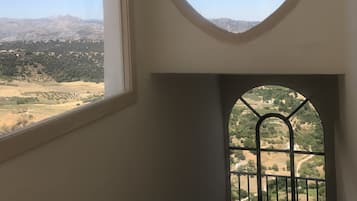 Een kamer met een groot raam en een kleiner rondboogvenster, beide met uitzicht op een bergachtig landschap.