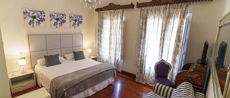 Une chambre d’hôtel avec un lit, un canapé, une chaise, un lustre et des rideaux.