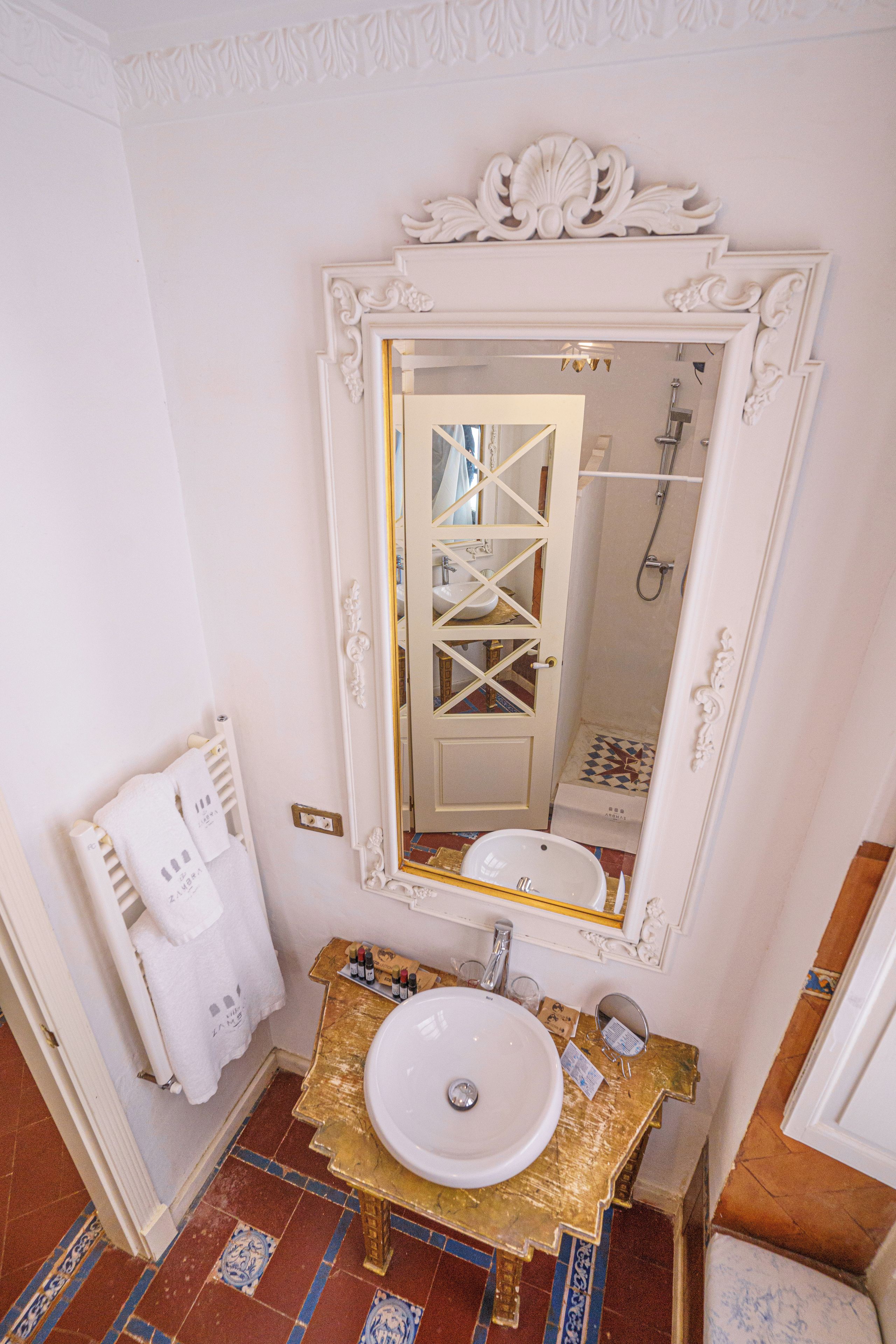 A bathroom with a white sink, a gold vanity, a large mirror, and a shower.