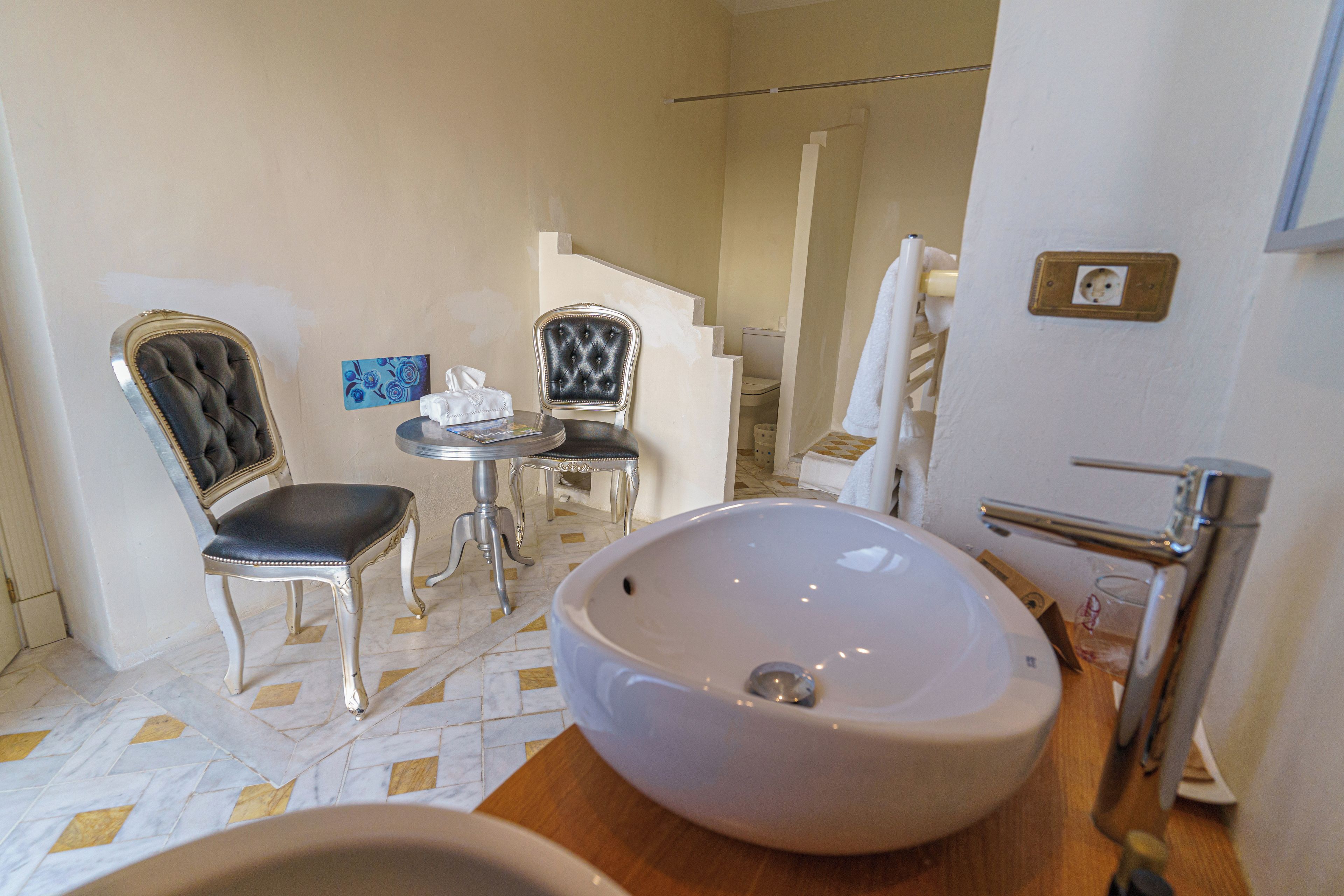 Une salle de bain avec un grand lavabo, deux chaises, une petite table et un porte-serviettes.