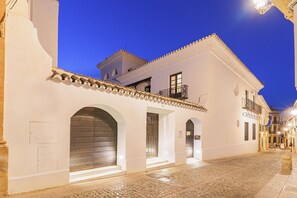 Un bâtiment historique donnant sur une rue pavée, avec des murs blancs et un balcon orné de balustrades en fer forgé.