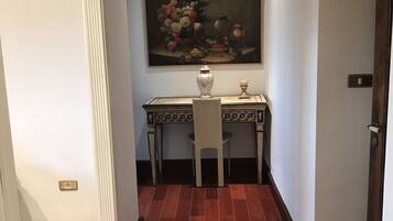 A hallway with a dining table and chairs, a vase, and a painting on the wall.
