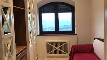 A bedroom with a large window, a red sofa, a patterned carpet, and a white wardrobe with a unique design.