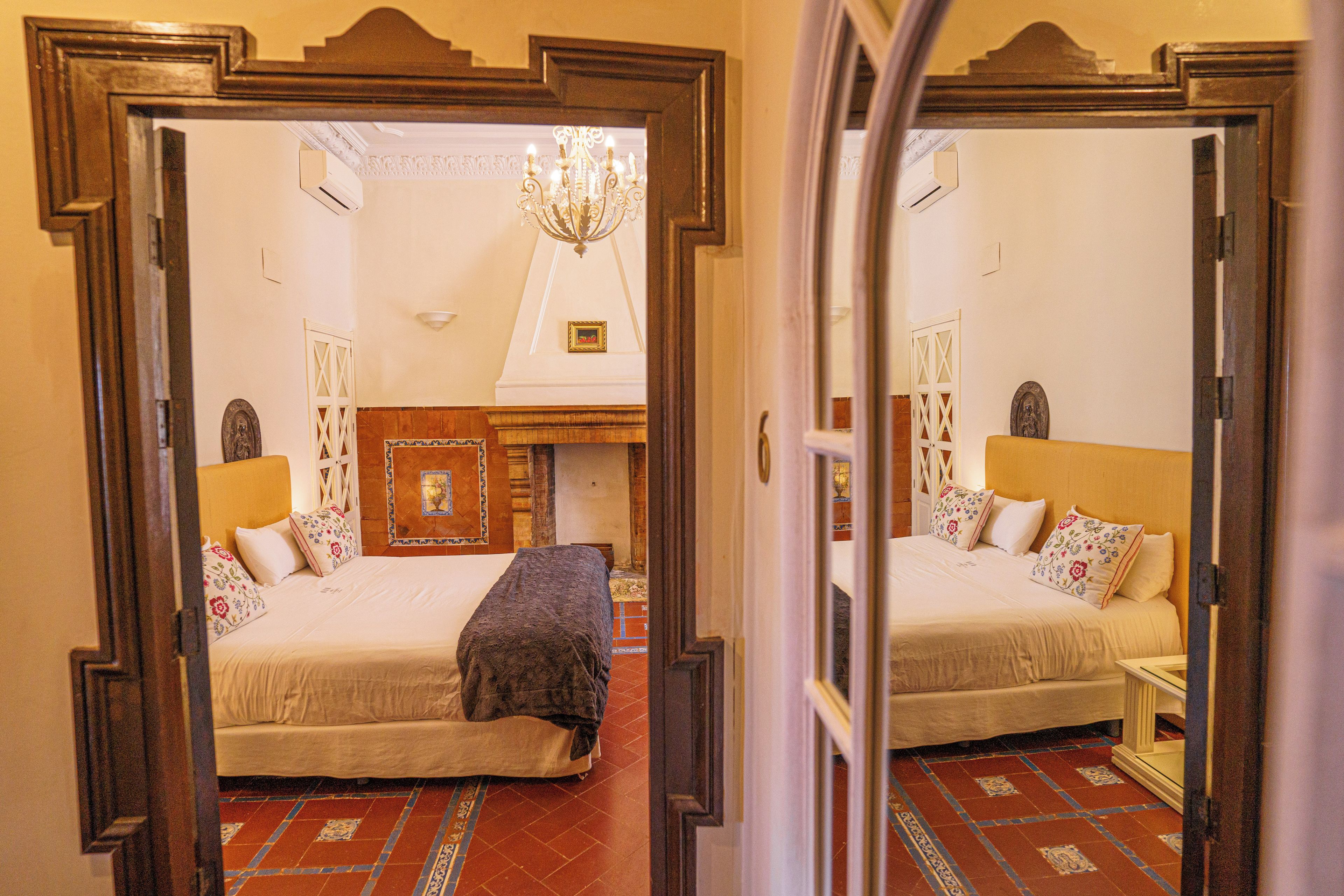 Una habitación con una cama grande, una cama más pequeña, un candelabro y una chimenea.