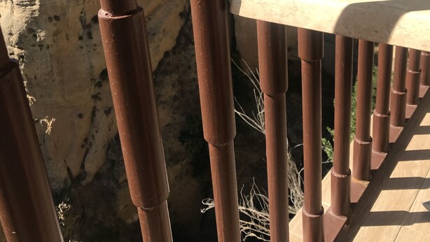 Un balcón con vista a un acantilado rocoso y edificios al fondo.