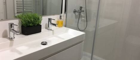 Une salle de bain moderne avec un lavabo blanc, un miroir, une petite plante et un espace douche.