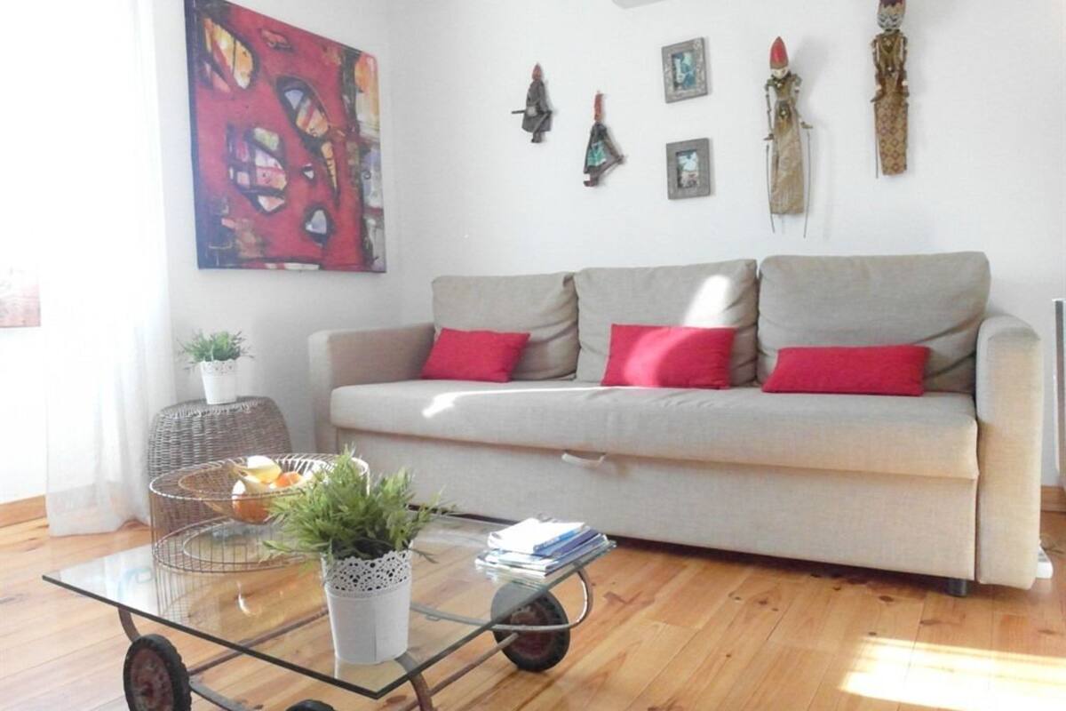 Un soggiorno con divano, cuscini rossi, tavolino in vetro con una pianta e una parete decorata con opere d'arte e ornamenti.