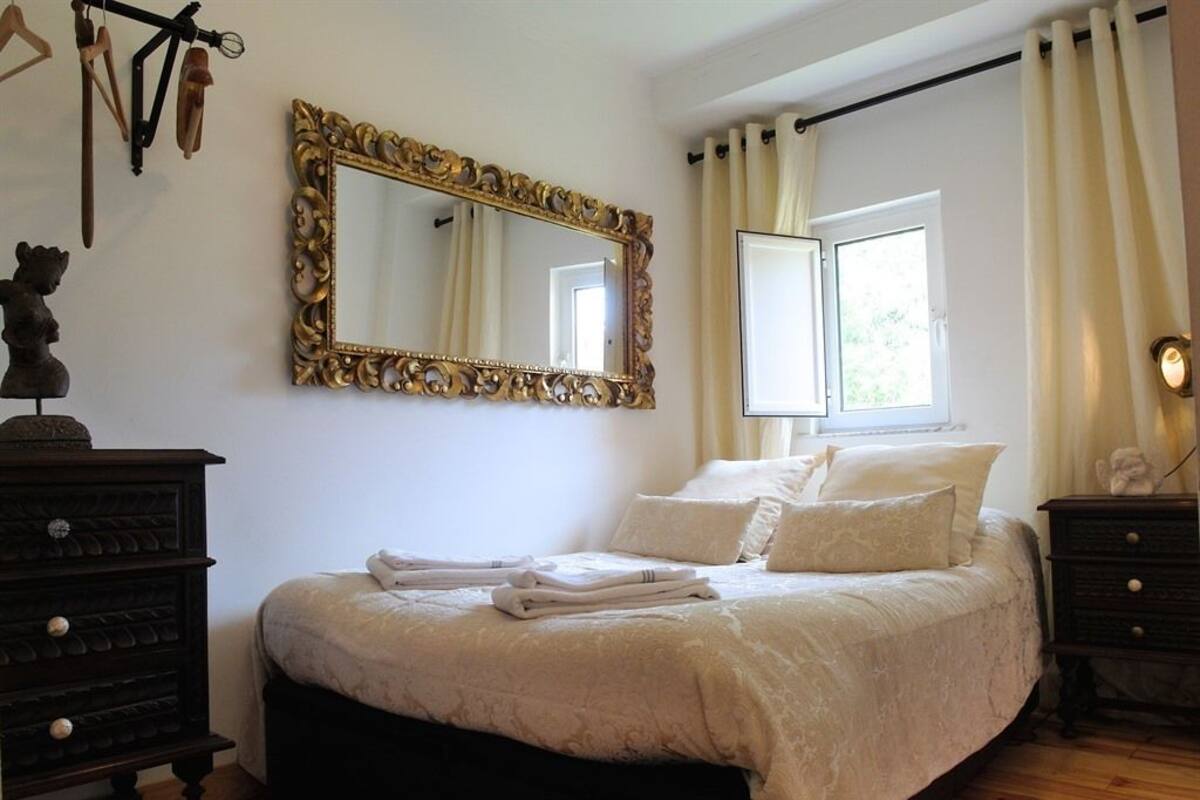 Una camera da letto con un grande specchio decorato, un letto con lenzuola bianche, un comò e una finestra con tende.