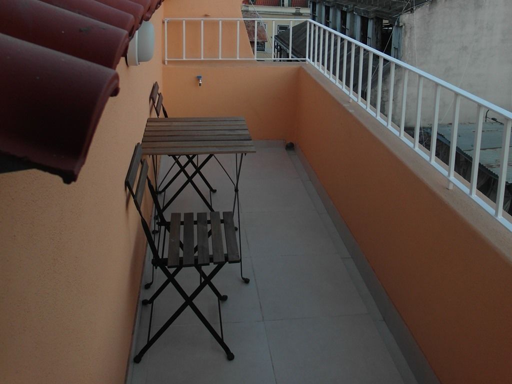 Een balkon met een metalen tafel en stoelen, een witte balustrade en uitzicht op omliggende gebouwen.