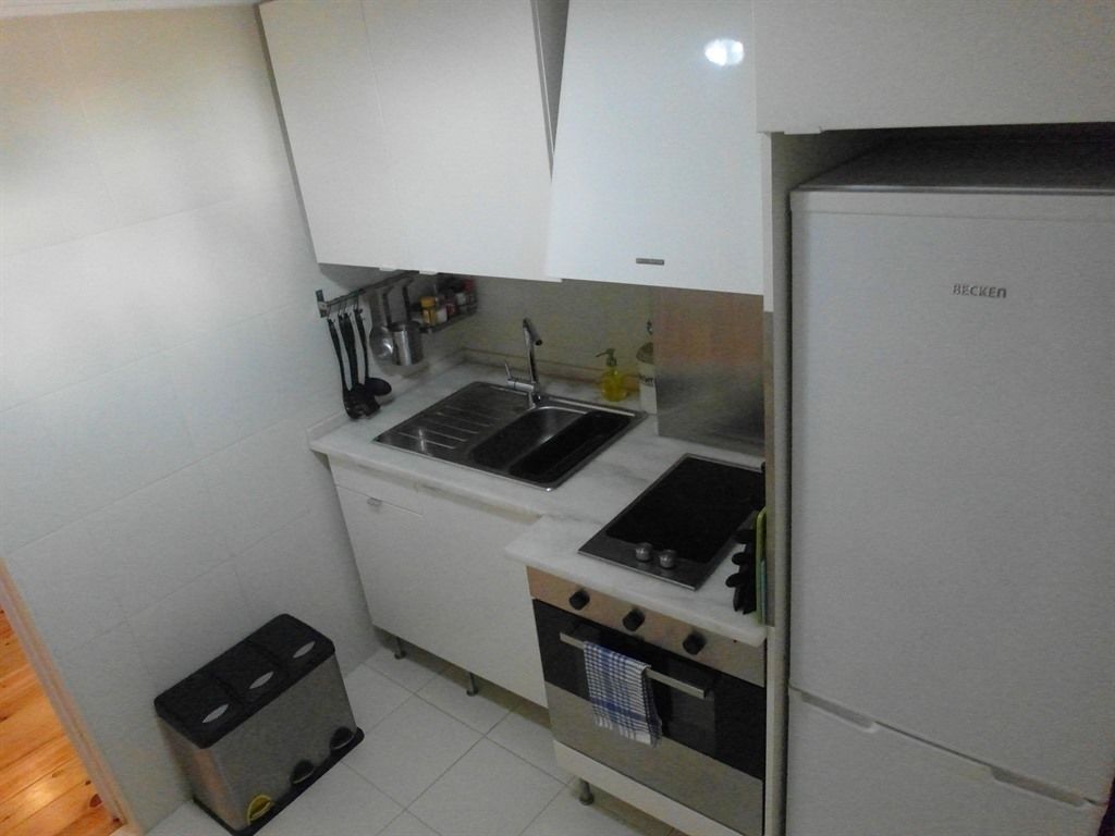 Une cuisine de taille réduite, avec des meubles blancs, un évier, une cuisinière et un réfrigérateur.