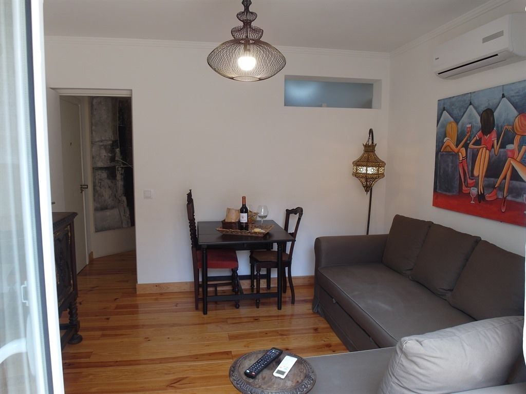 Un salon avec un canapé gris, une table à manger avec des chaises, un lustre et un tableau accroché au mur.