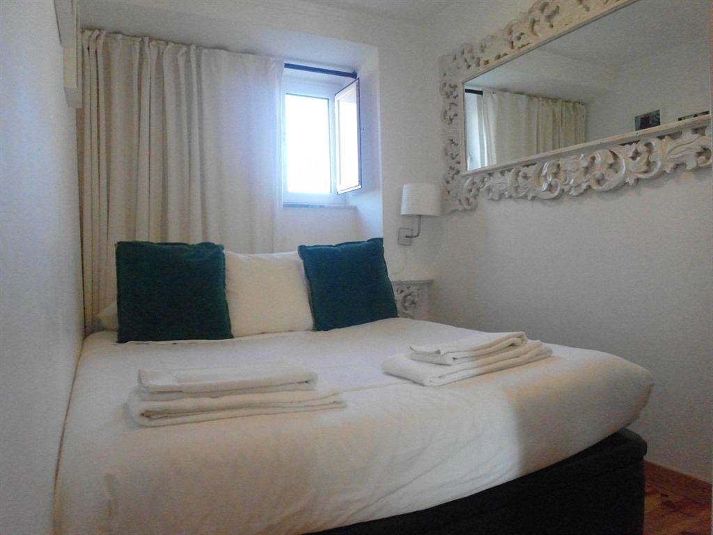 A neatly made bed with white linens and two pillows, a window with curtains, and a mirror with an ornate frame.