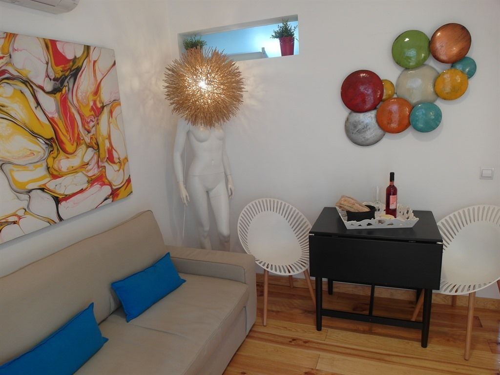 Ein modernes Wohnzimmer mit einem beigen Sofa, blauen Kissen, einem weißen Sessel, einem schwarzen Tisch mit einer Flasche und einem farbenfrohen abstrakten Gemälde.
