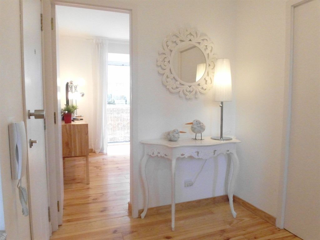 A room with a wooden floor, a white table with a lamp and decorative items, and a mirror on the wall.