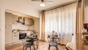A modern kitchen with a dining area, featuring a wooden floor, a ceiling fan, and a large window with curtains. - AwesHome - Vintage Rooms (Pisa)