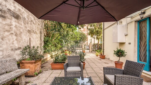 An outdoor patio area with a table and chairs, surrounded by potted plants and a large umbrella. - AwesHome - Vintage Rooms (Pisa)