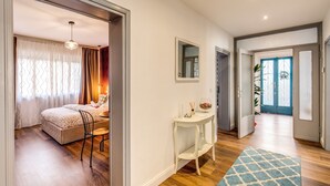 A hotel room with a bed, a small table, and a chair. There is a door leading to another room and a window with curtains. - AwesHome - Vintage Rooms (Pisa)