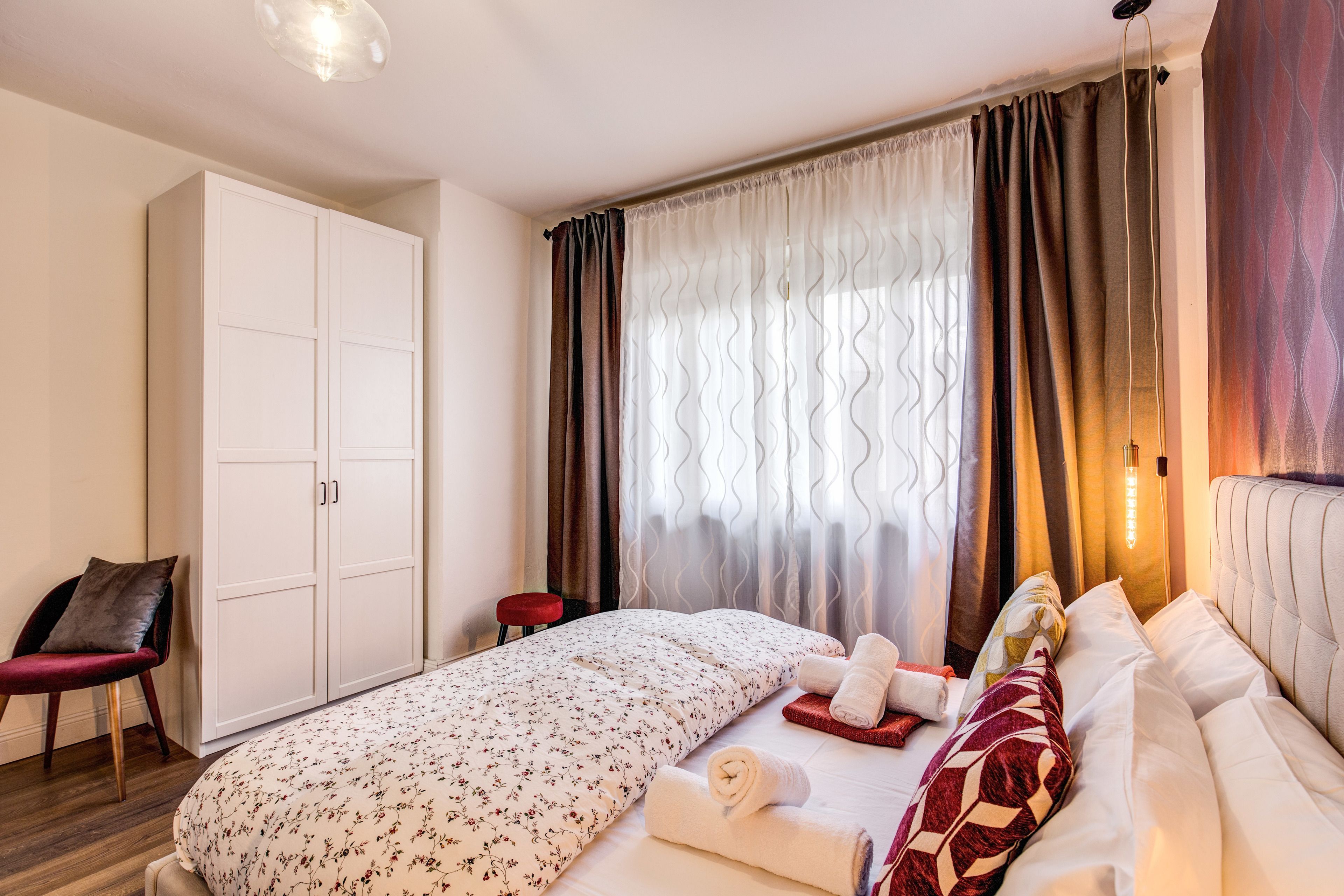 Una camera d'albergo con un letto, un armadio, una sedia e uno sgabello.