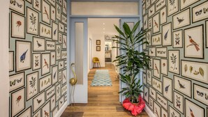 A hallway with framed botanical and avian artwork on the walls, a potted plant, and a golden floor lamp. - AwesHome - Vintage Rooms (Pisa)