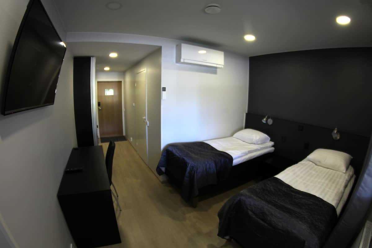 A hotel room with two beds, a TV, a desk, and an air conditioning unit.