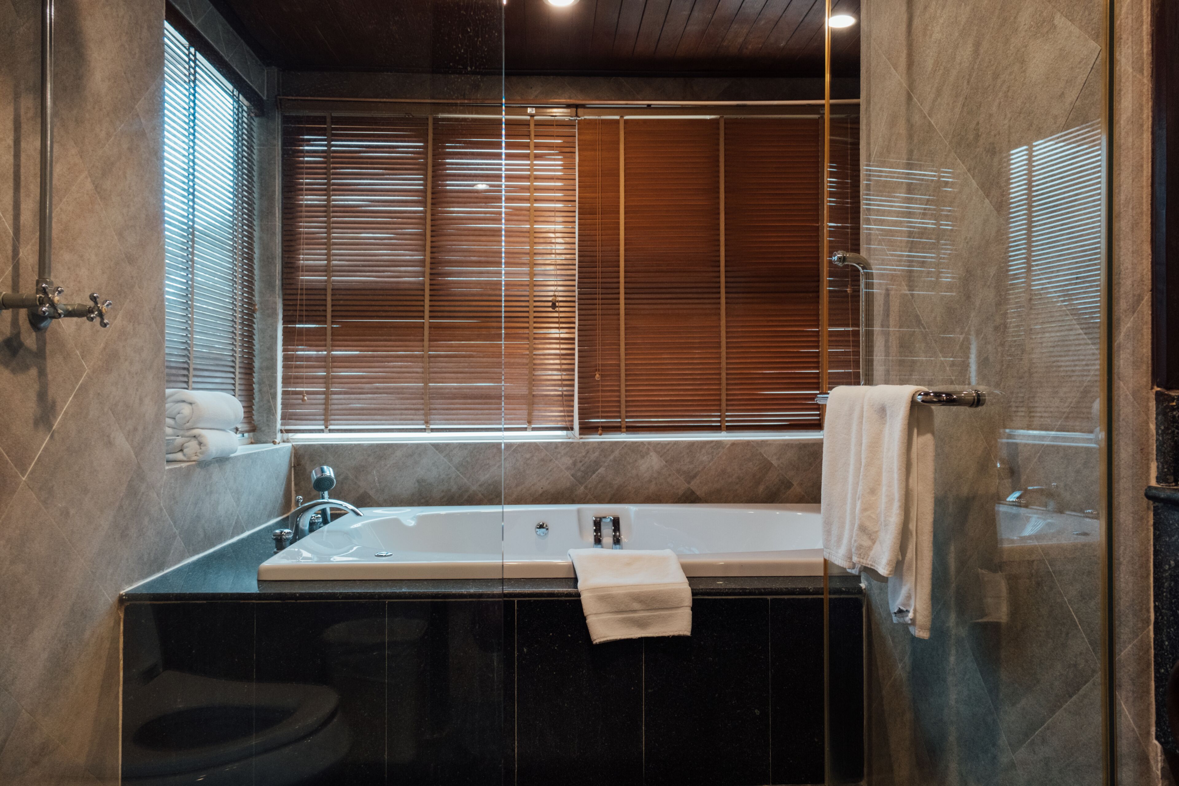 A bathroom with a bathtub, toilet, and window with blinds.
