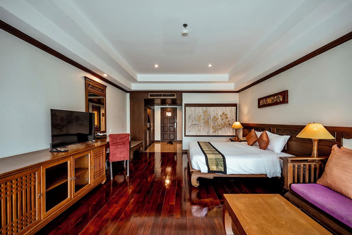 Una habitación de hotel con piso de madera, televisor, cama con almohadas, sofá y lámpara.