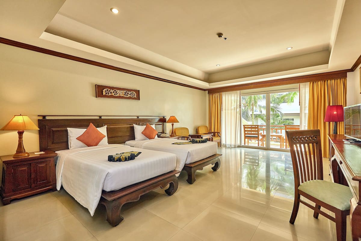 Habitación de hotel con dos camas, televisión, escritorio y vistas a palmeras.