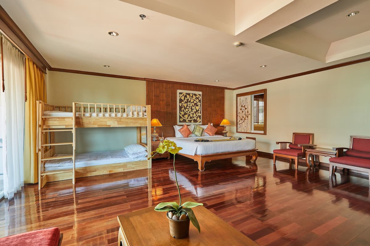 Habitación de hotel con literas, una cama grande, un escritorio, una silla y una planta en maceta.