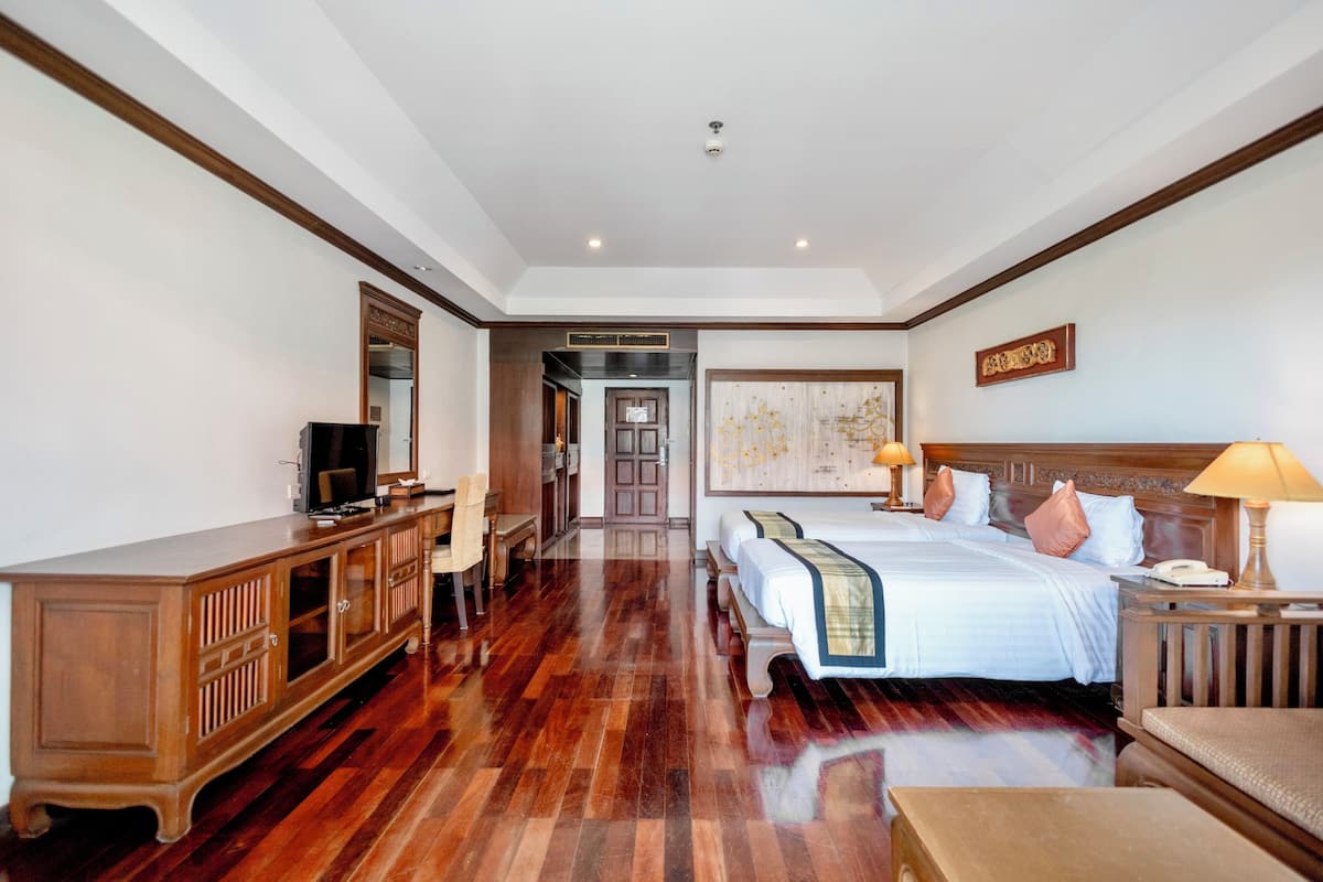 Habitación de hotel con suelo de madera, una cama con dos almohadas, un escritorio con silla, televisor y un cuadro en la pared.