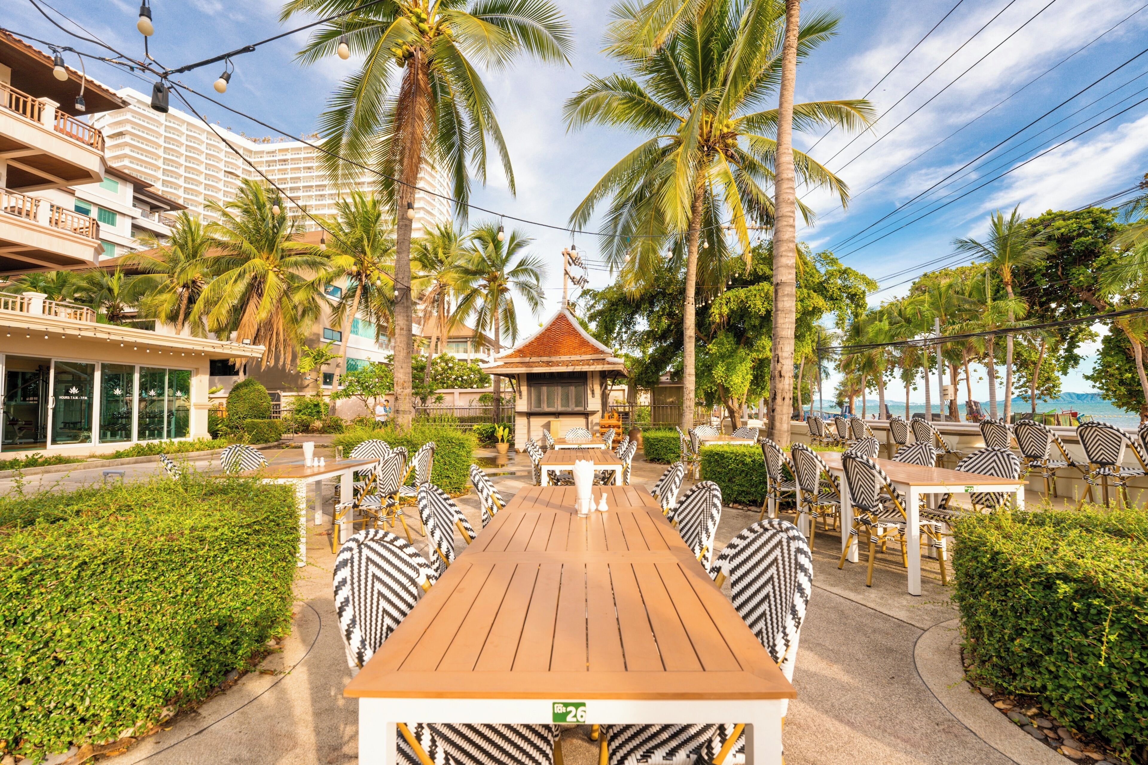 A resort with outdoor dining, palm trees, and a view of the sea.