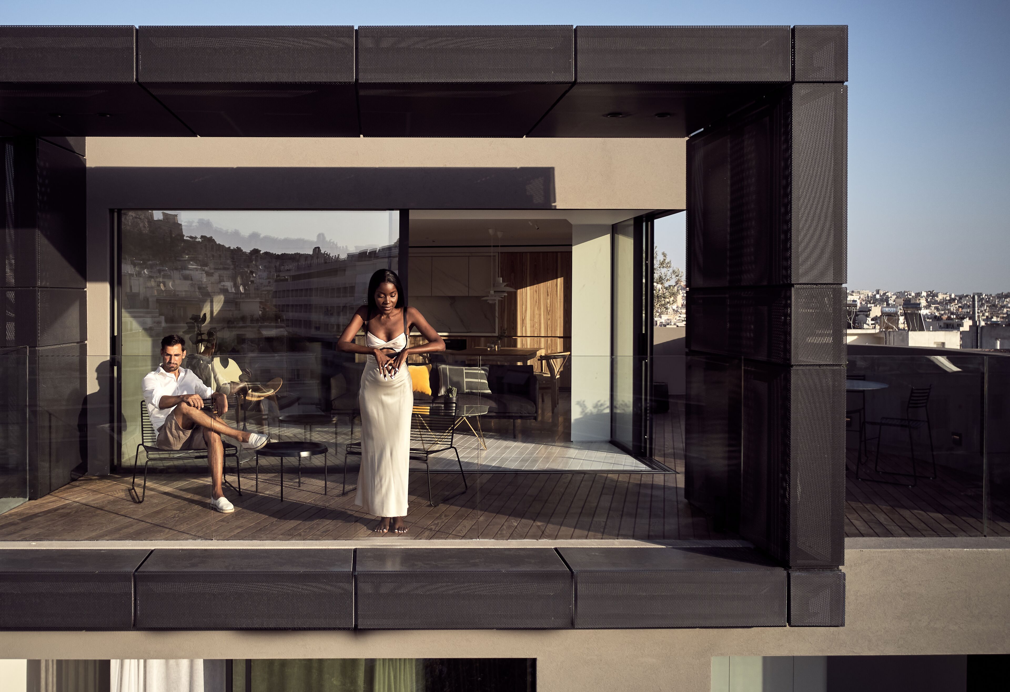 A modern building with a glass facade, a patio area with outdoor furniture, and a view of the cityscape.