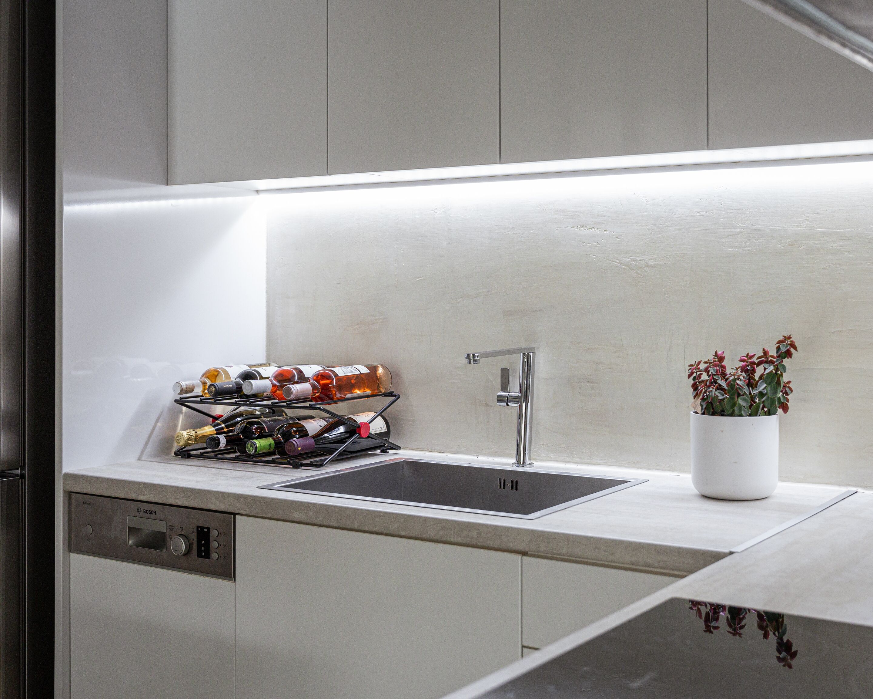 Eine moderne Küche mit integriertem Geschirrspüler, einer Edelstahl-Spüle und einem Weinkühlschrank mit verschiedenen Flaschen.