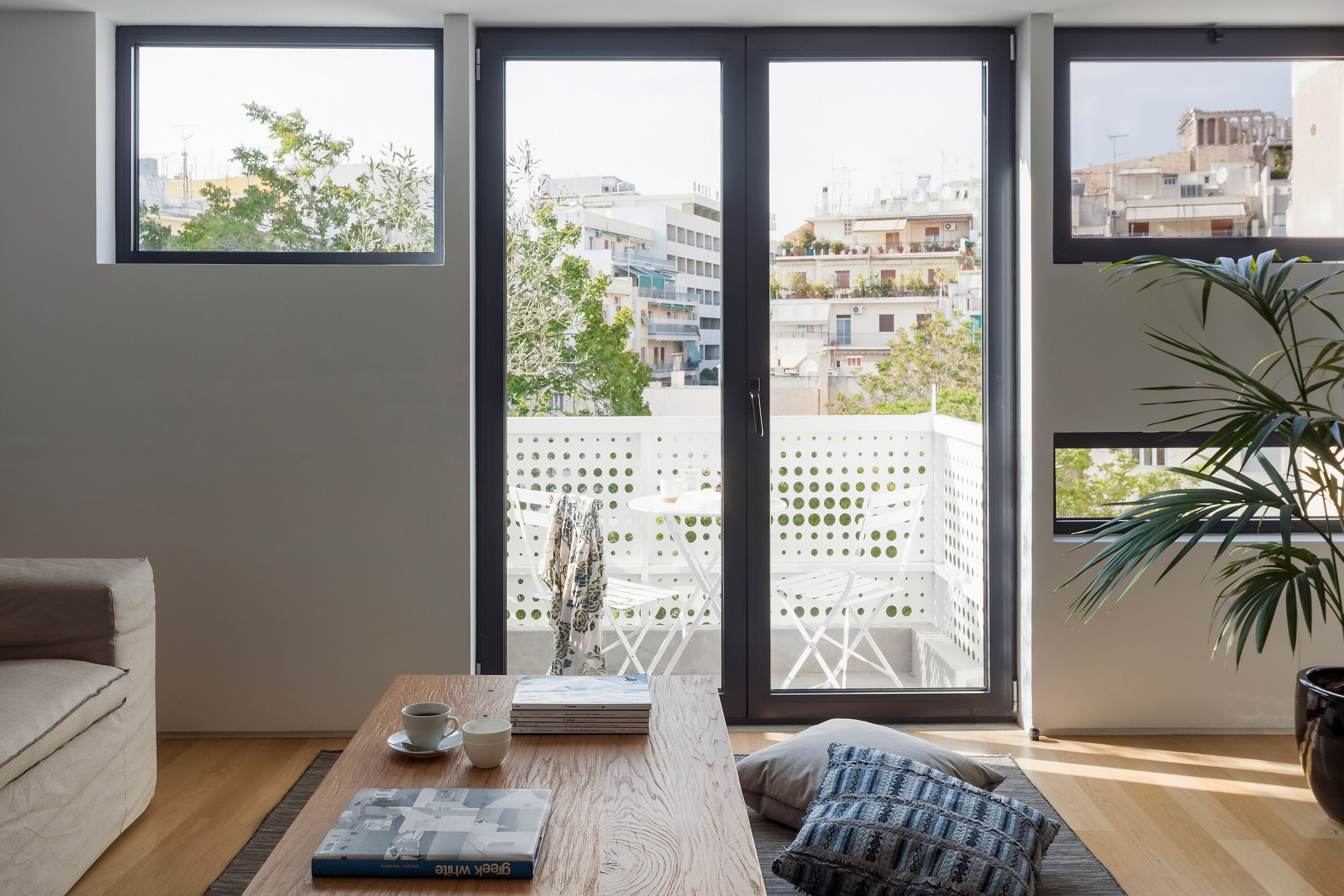A modern living room with a large sliding glass door leading to a balcony, a wooden coffee table with a book and a cup, and a potted plant.