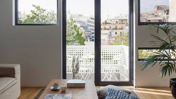 A modern living room with a large sliding glass door leading to a balcony, a wooden coffee table with a book and a cup, and a potted plant.