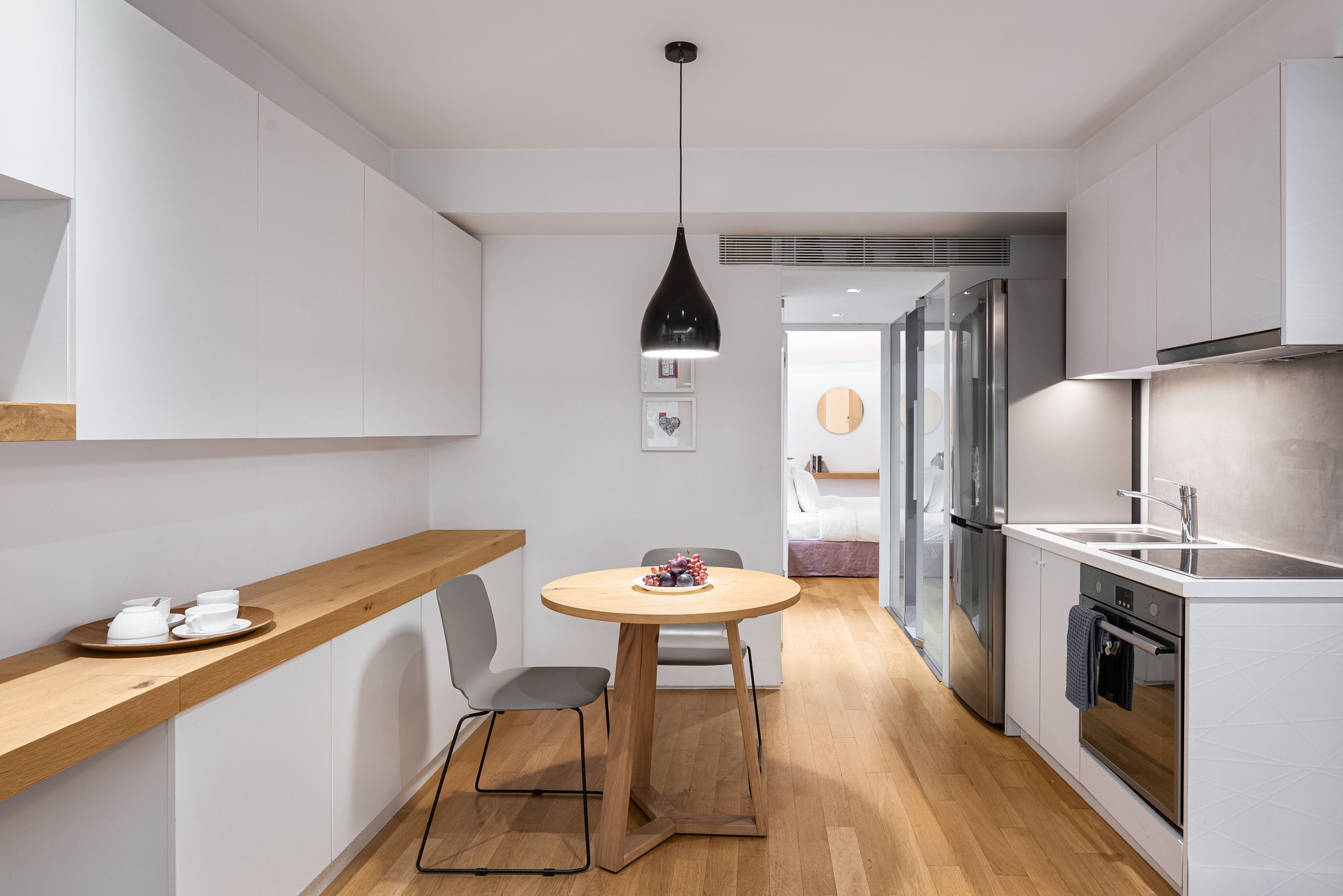 A modern kitchen with white cabinetry, a wooden countertop, a round dining table, and a black pendant light.