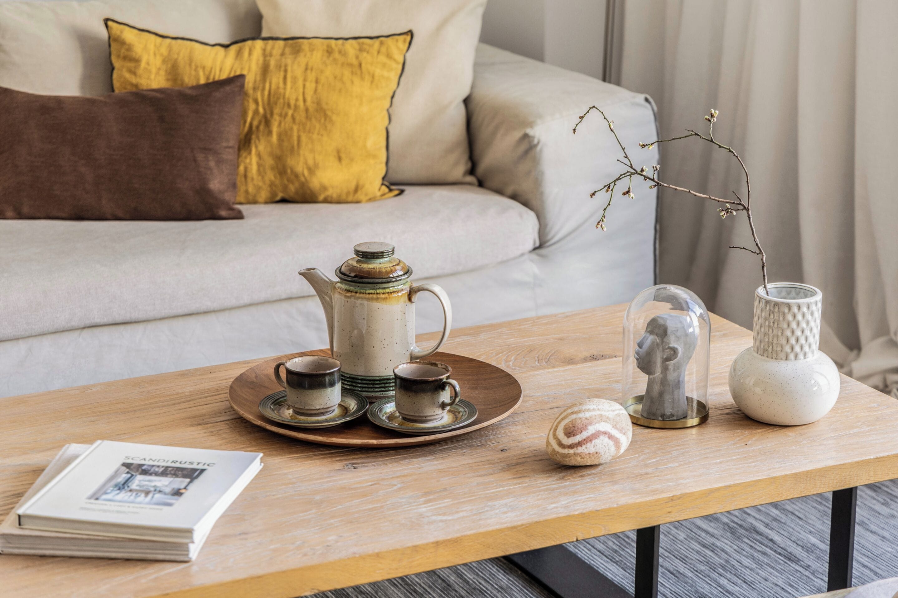 Uma mesa de centro de madeira com uma chaleira, xícaras, um vaso decorativo e um livro.